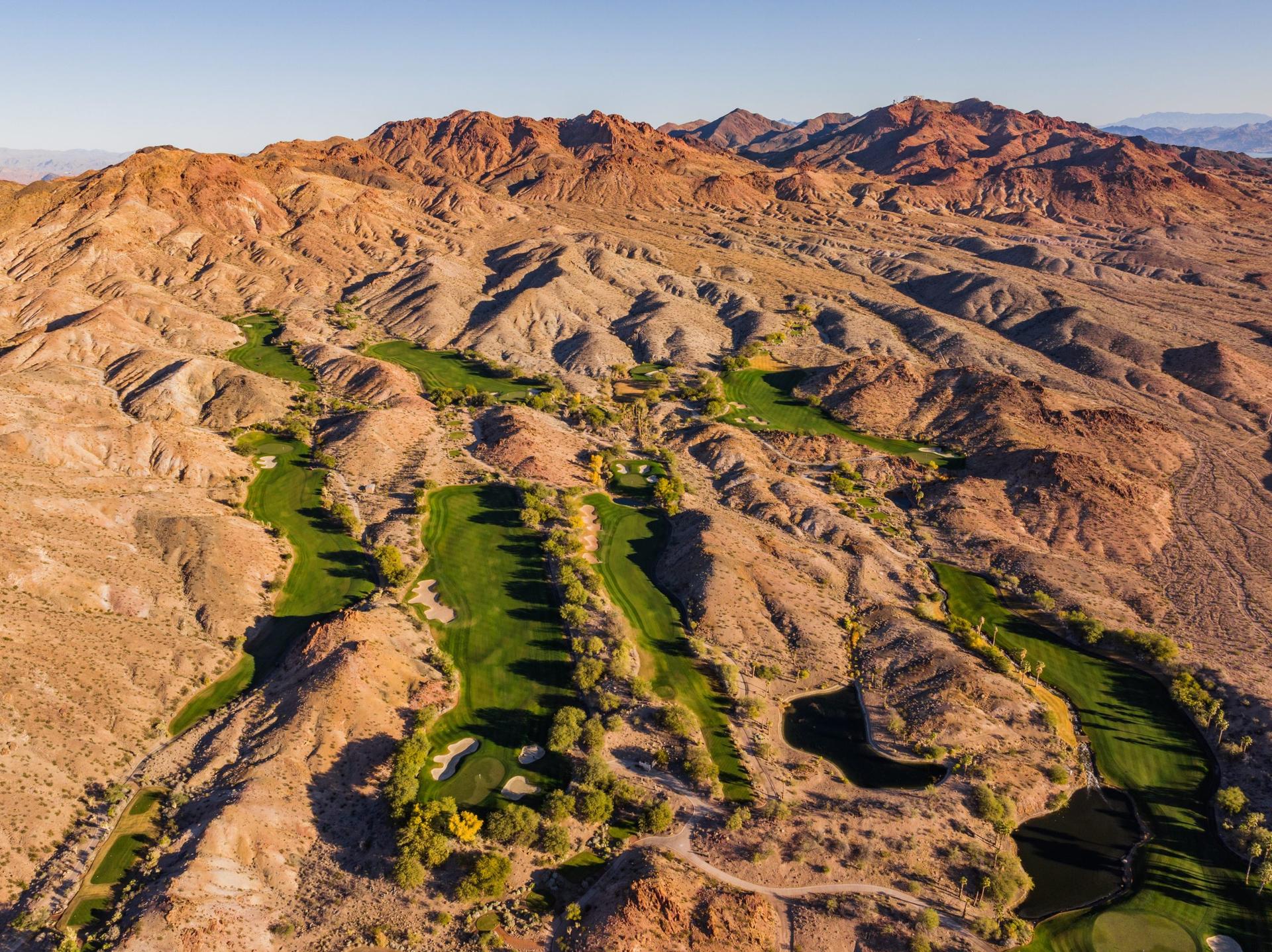 Aerial view of a lush golf course nestled between rugged desert mountains