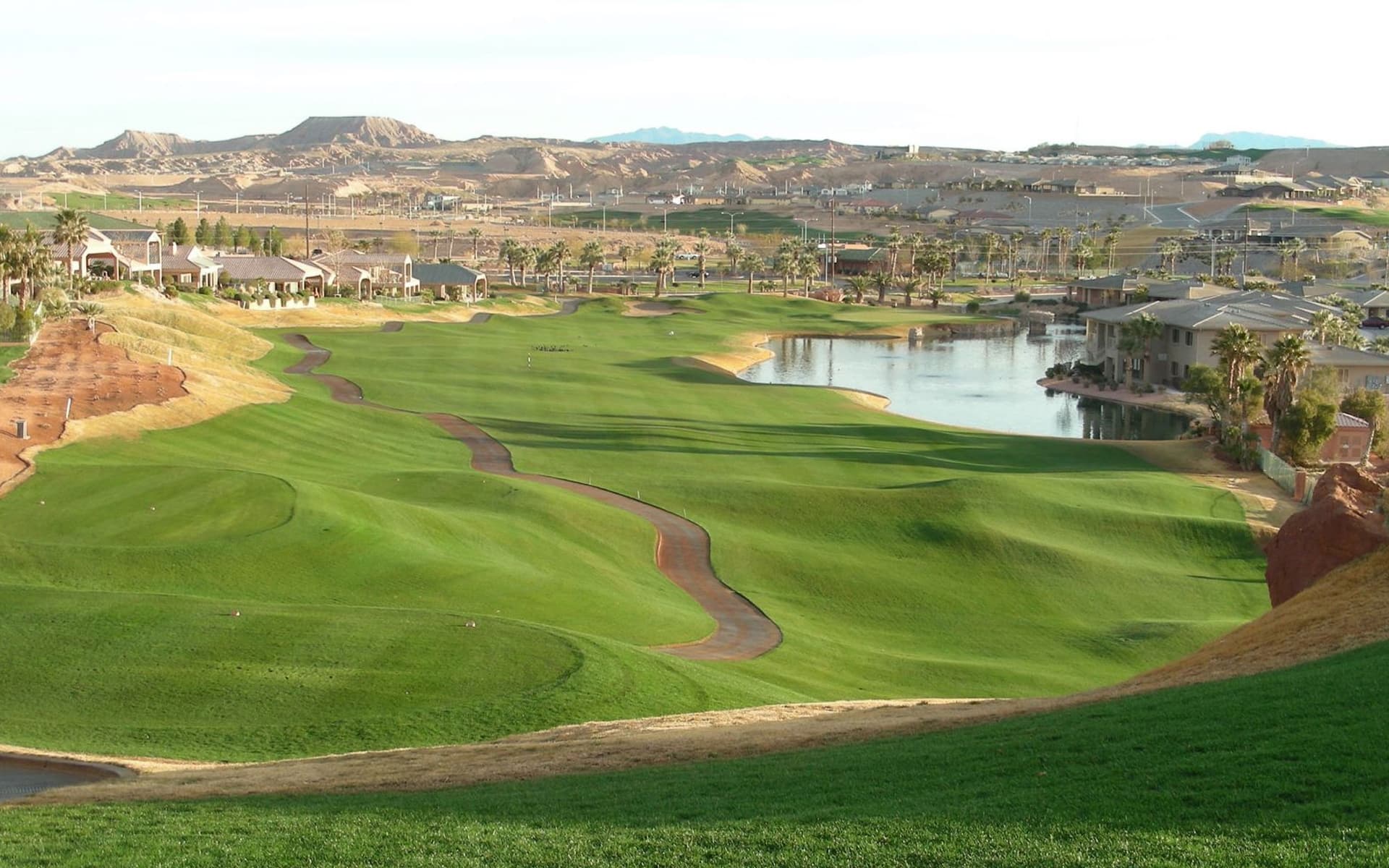 A wide fairway next to a water hazard with a concrete walk path