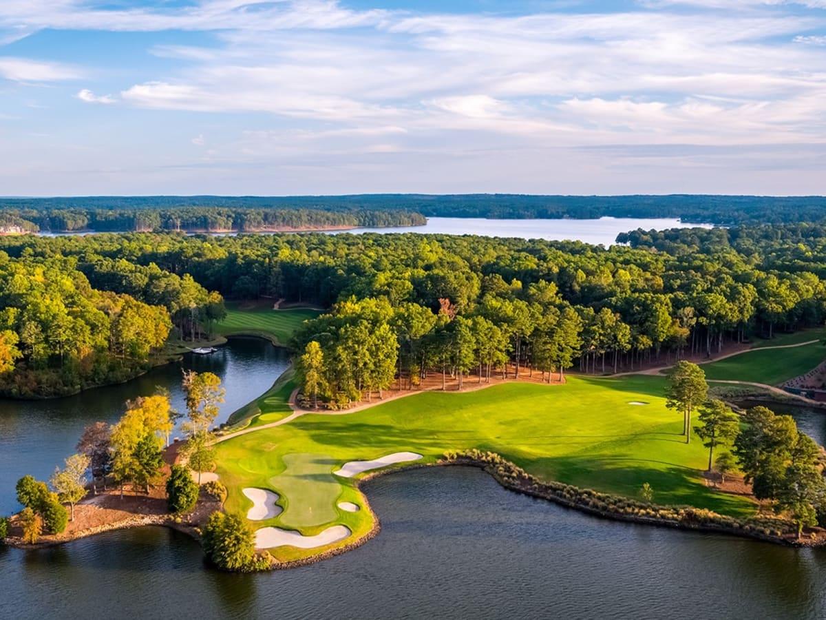 An aerial view of a golf course with fairways and greens weaving around a lake.
