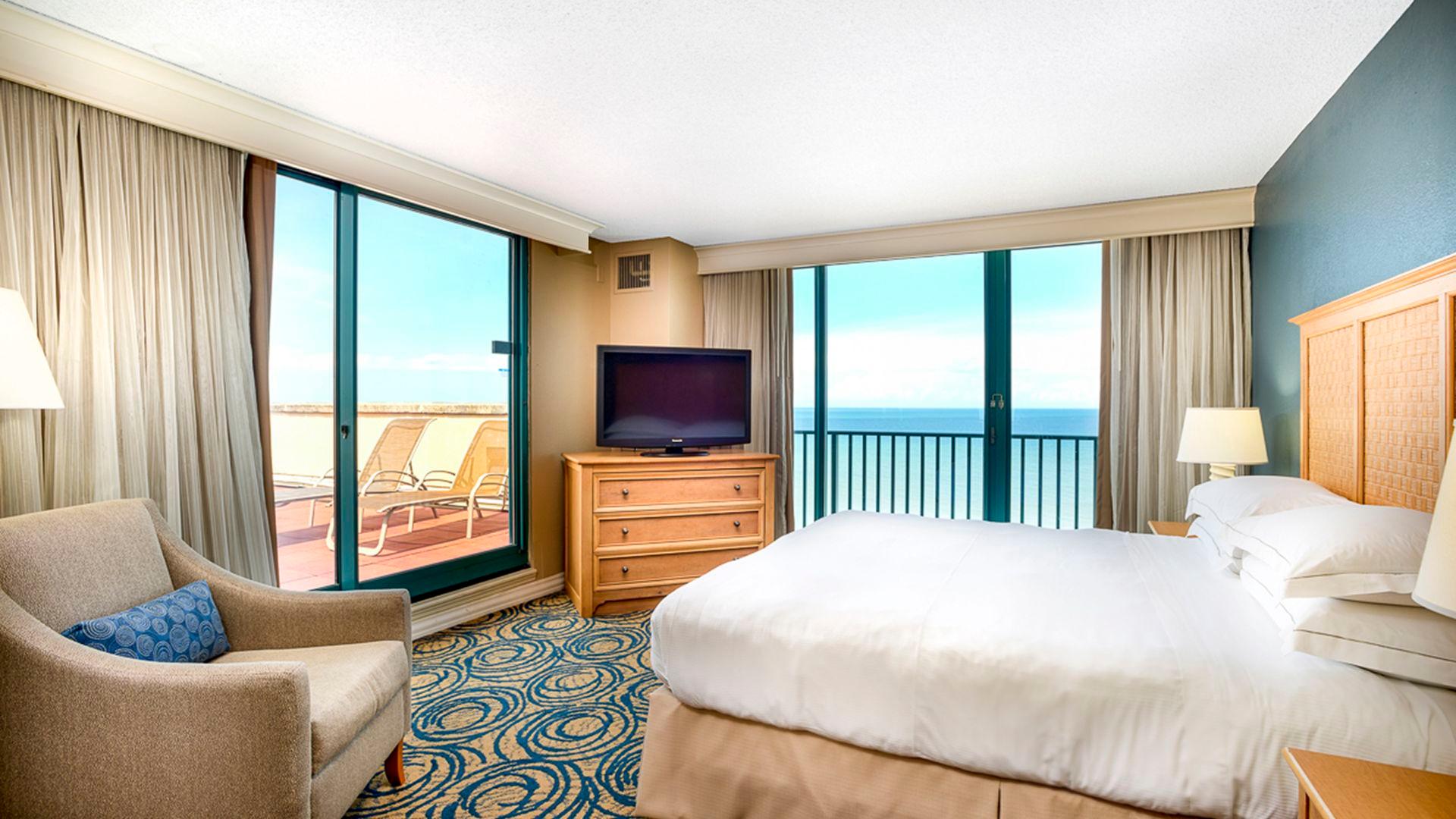 Double bed room with balcony views of the ocean and a patio equipped with sun beds