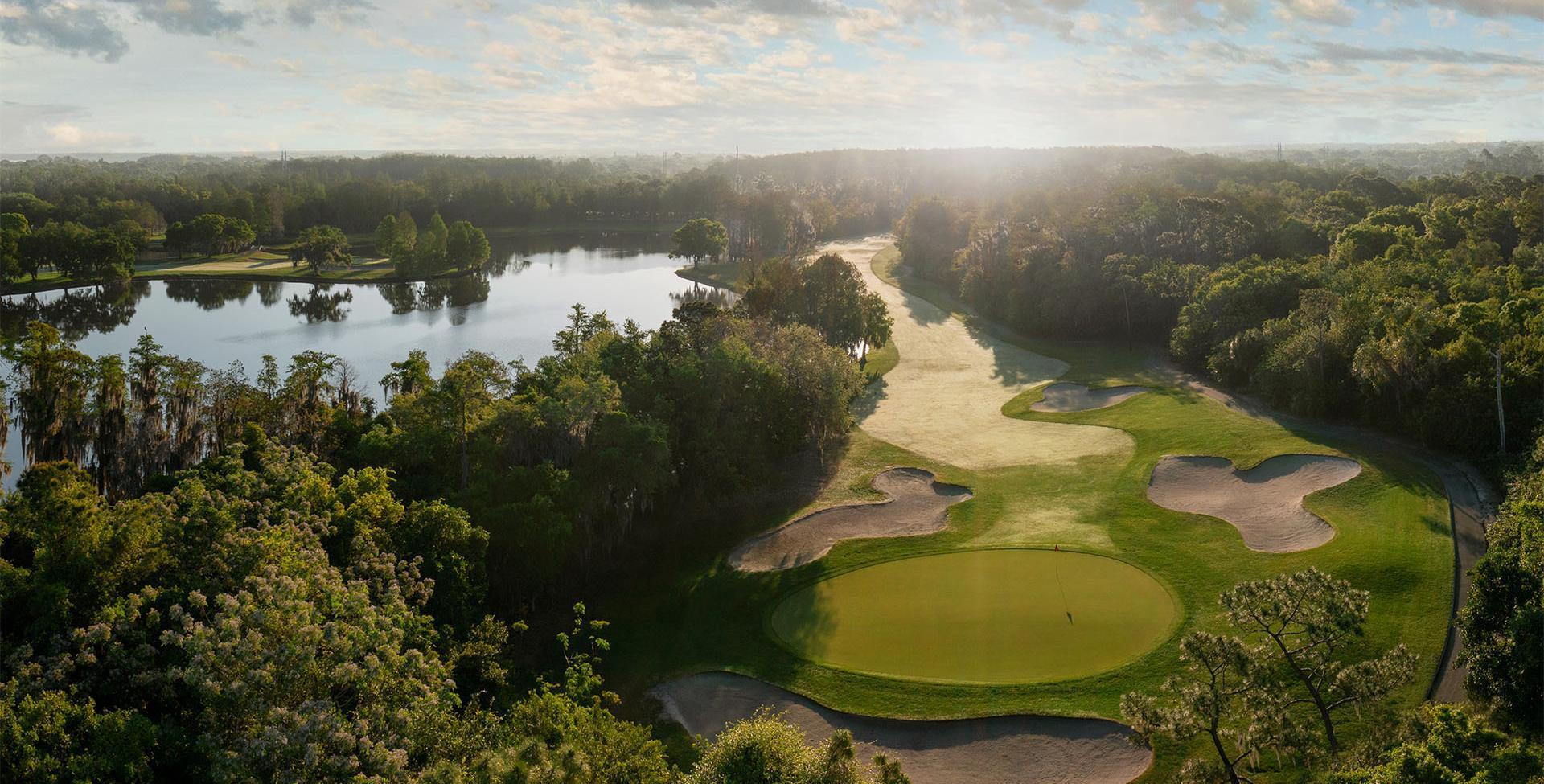 A misty morning view of a lakeside fairway with perfectly placed bunkers amidst a dense forest.