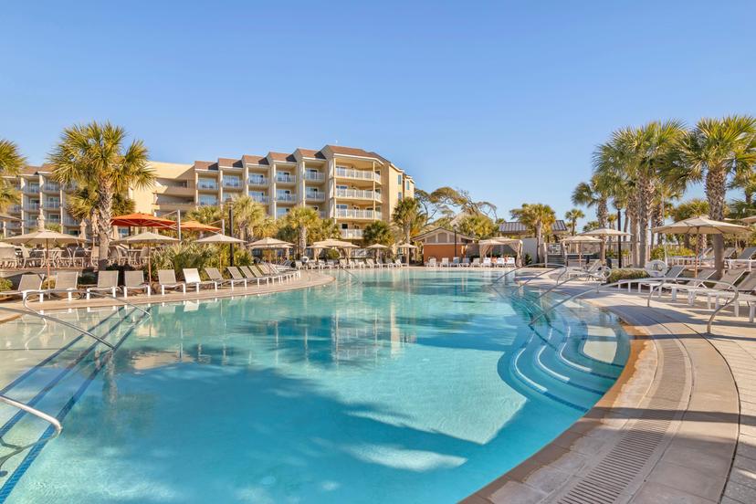 Panoramic view the resort building towering over a swimming pool surrounded by sunbeds