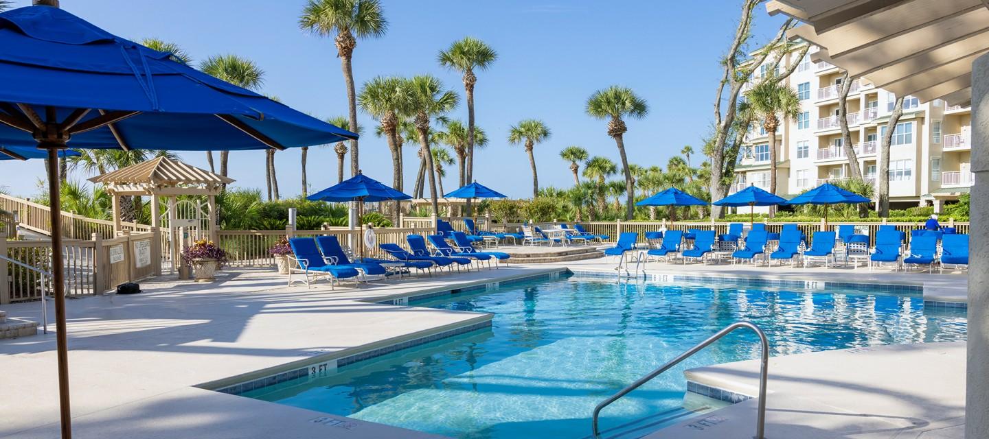 Swimming pool at the resort surrounded by blue sunbeds and umbrellas