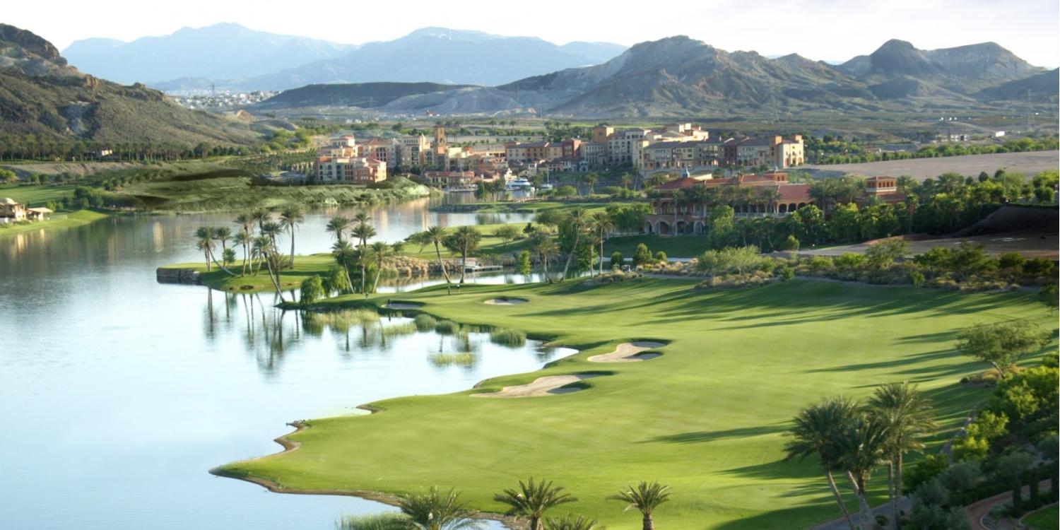 Scenic desert golf course with expansive lakes and elegant resort buildings framed by towering mountains.