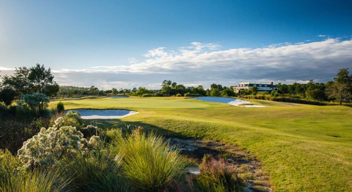 Panoramic view of a fairway leading to manicured greens with the clubhouse in the distance