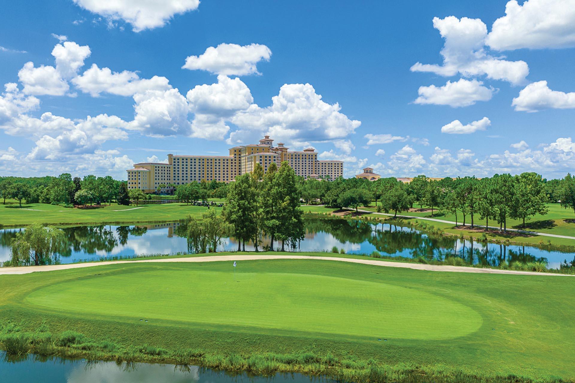 A pristine green beside a reflective lake with a luxury resort in the background.