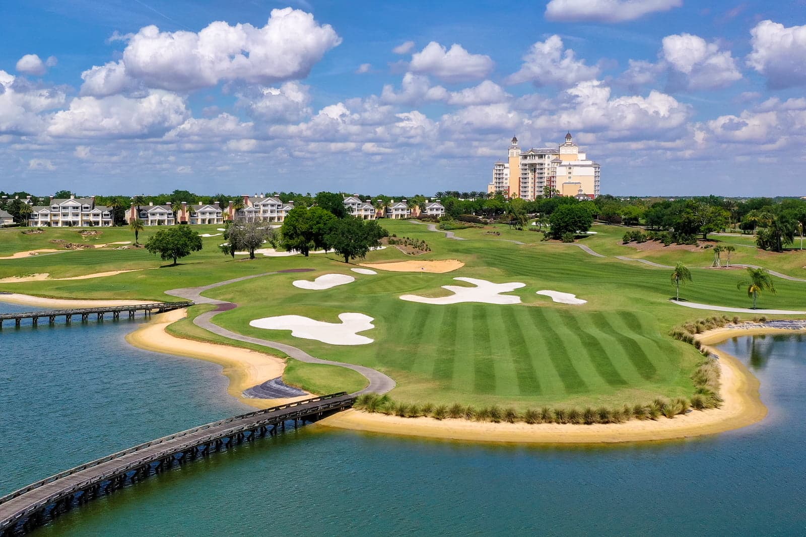A scenic course with wide fairways and a bridge over water leading to the green.