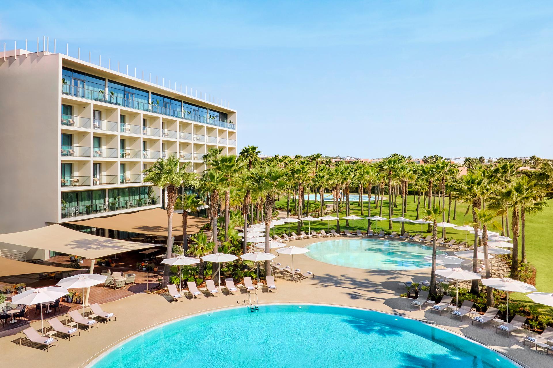 Outdoor swimming pool area with palm trees overlooked by the hotel