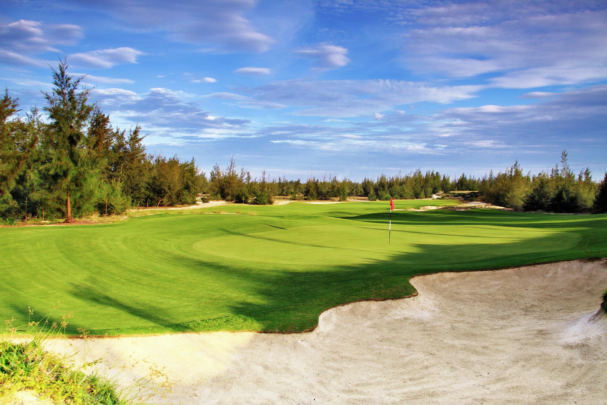 A large sand bunker strategically placed by a manicured green at the BRG Da Nang Golf Resort