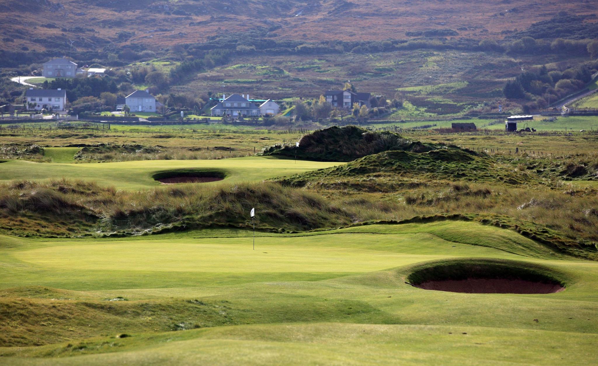 Wide angle shot of the greens with surrounding bunkers and long grass on the landscape