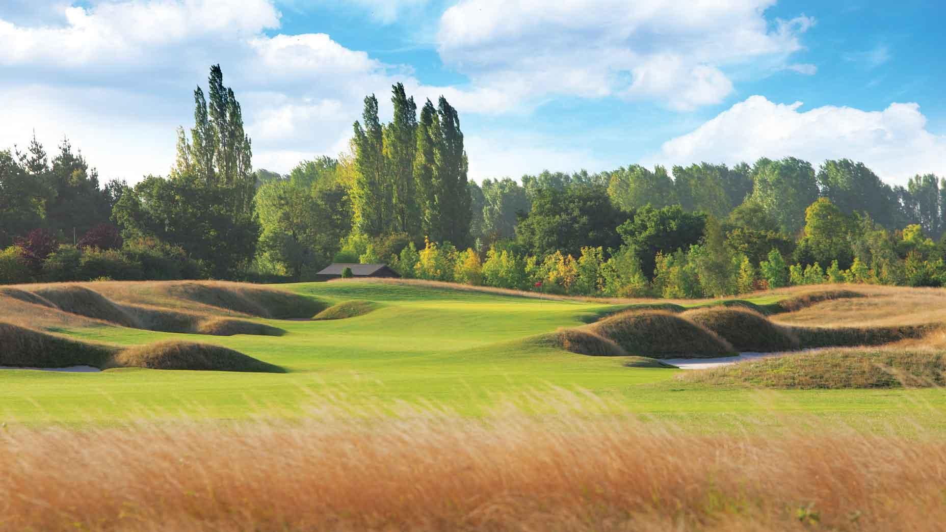 Rolling dunes and a yellow rough surrounding the manicured green under blue skies at The Belfry vourse