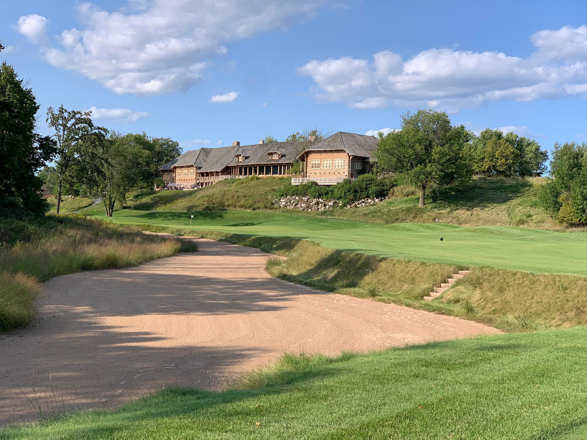 Historic golf clubhouse overlooking a challenging bunker and lush fairway.