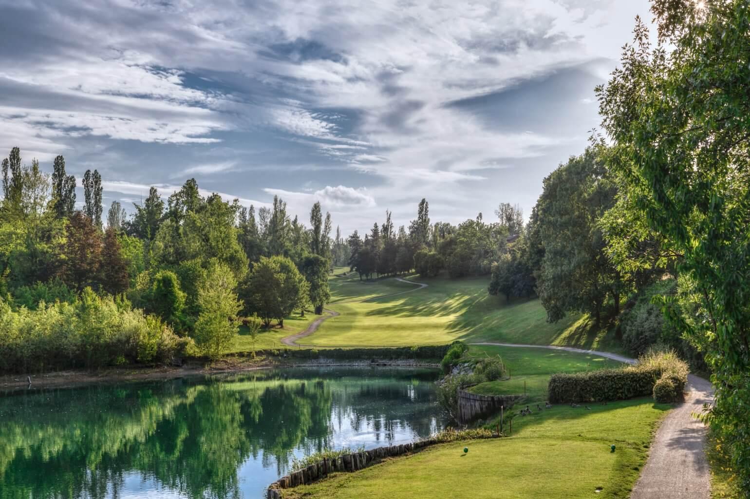 A serene golf fairway running along a reflective lake with trees on both sides.