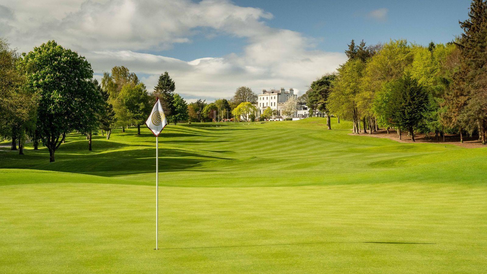 A pin flag stands tall with the clubhouse visible in the background.