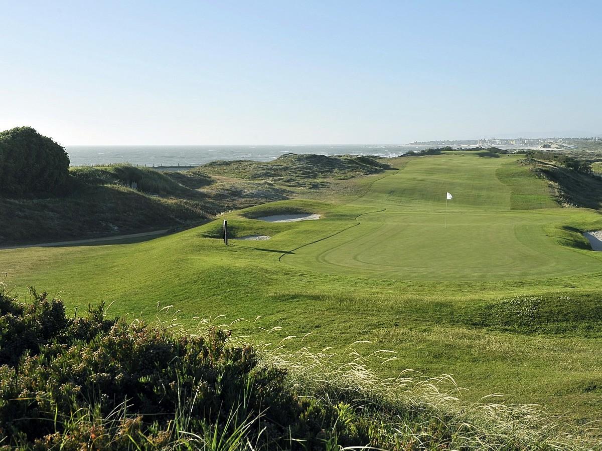 Narrow fairway leading up to a sloping green with the ocean in the background
