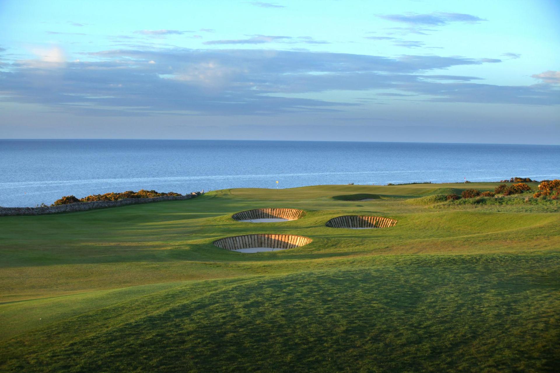 A stunning links golf course with pot bunkers overlooking the calm blue sea.