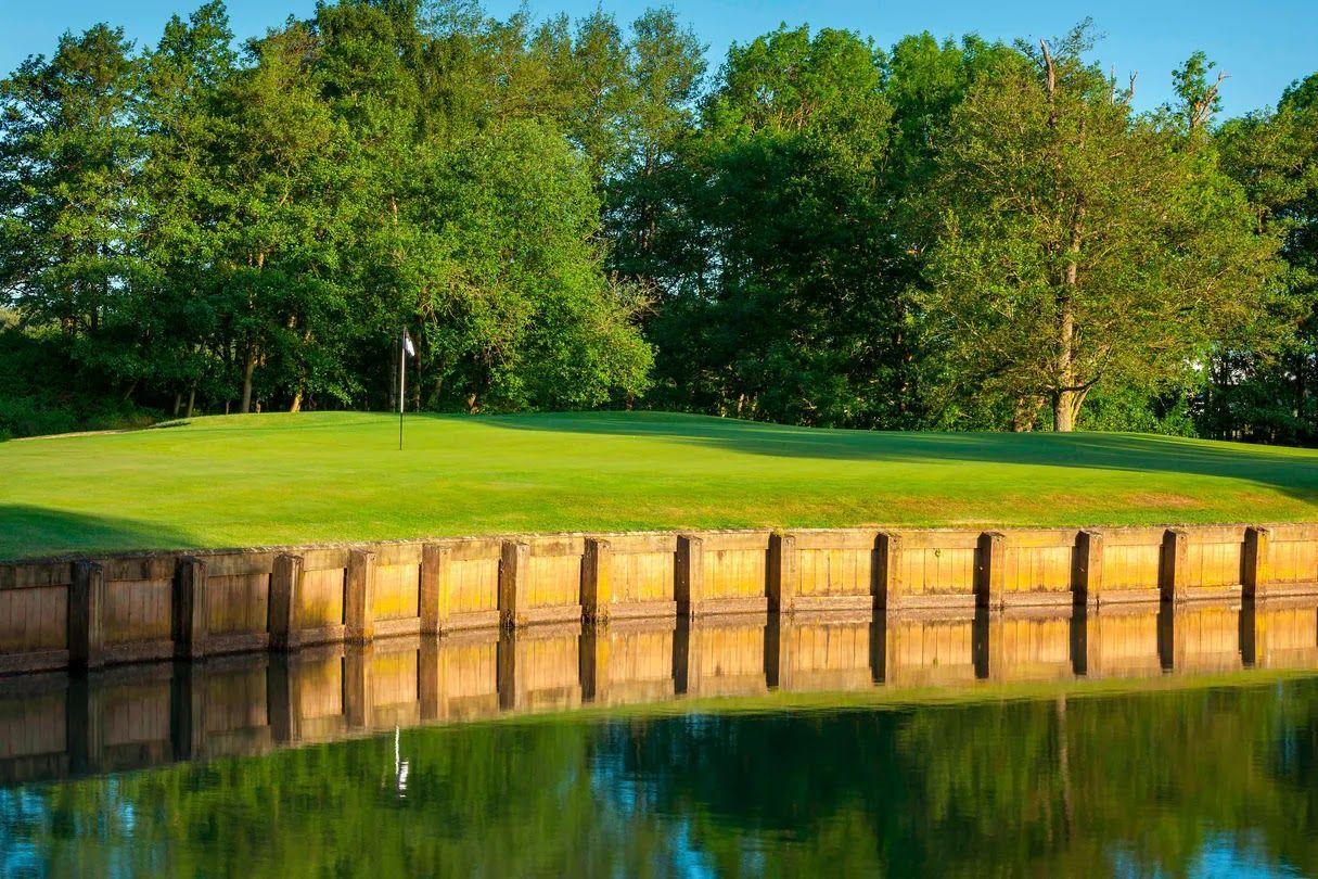 Green bordered by wooden retaining wall over water.