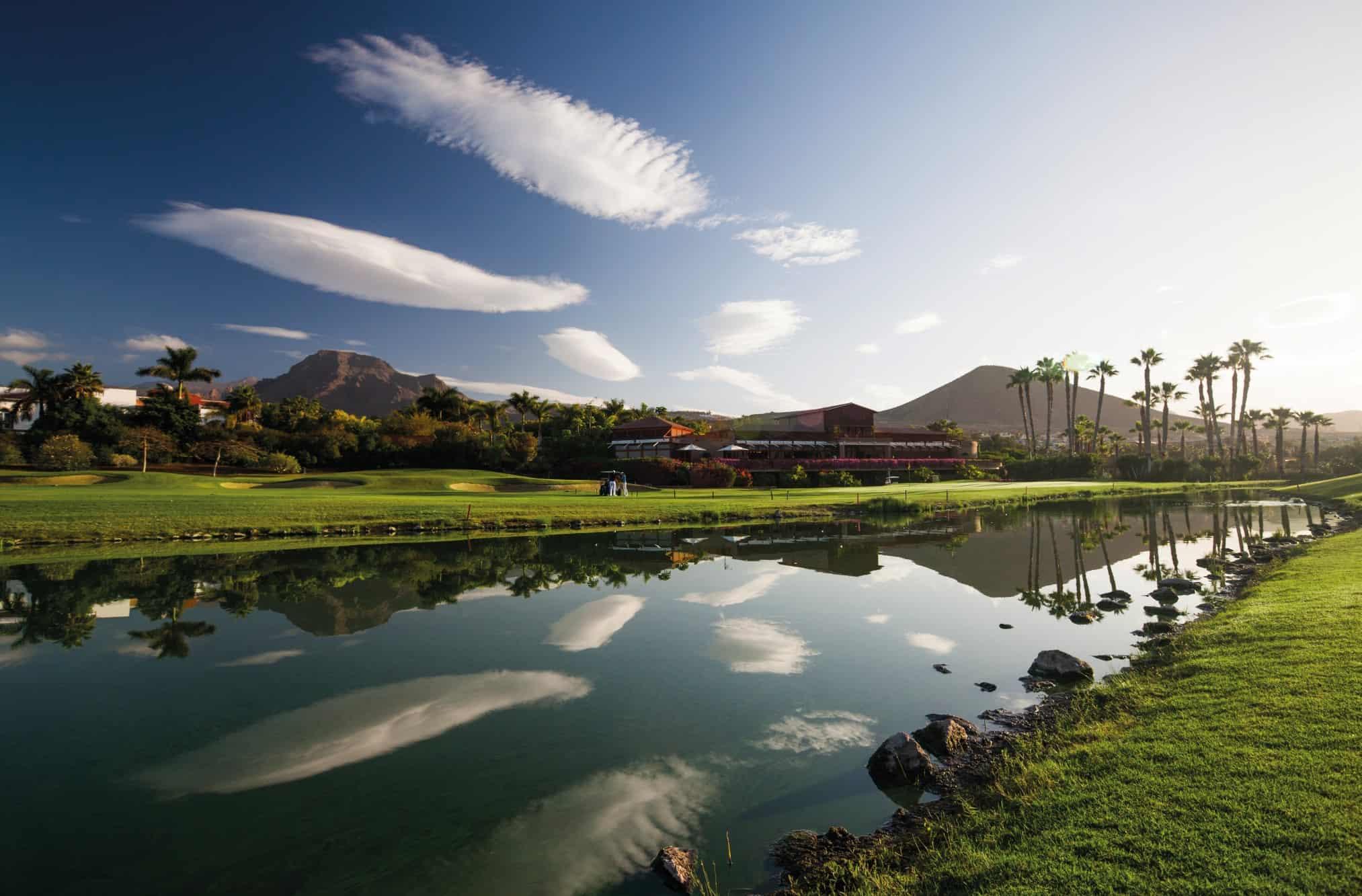 Water hazard running alongside pristine fairway, clubhouse in the background