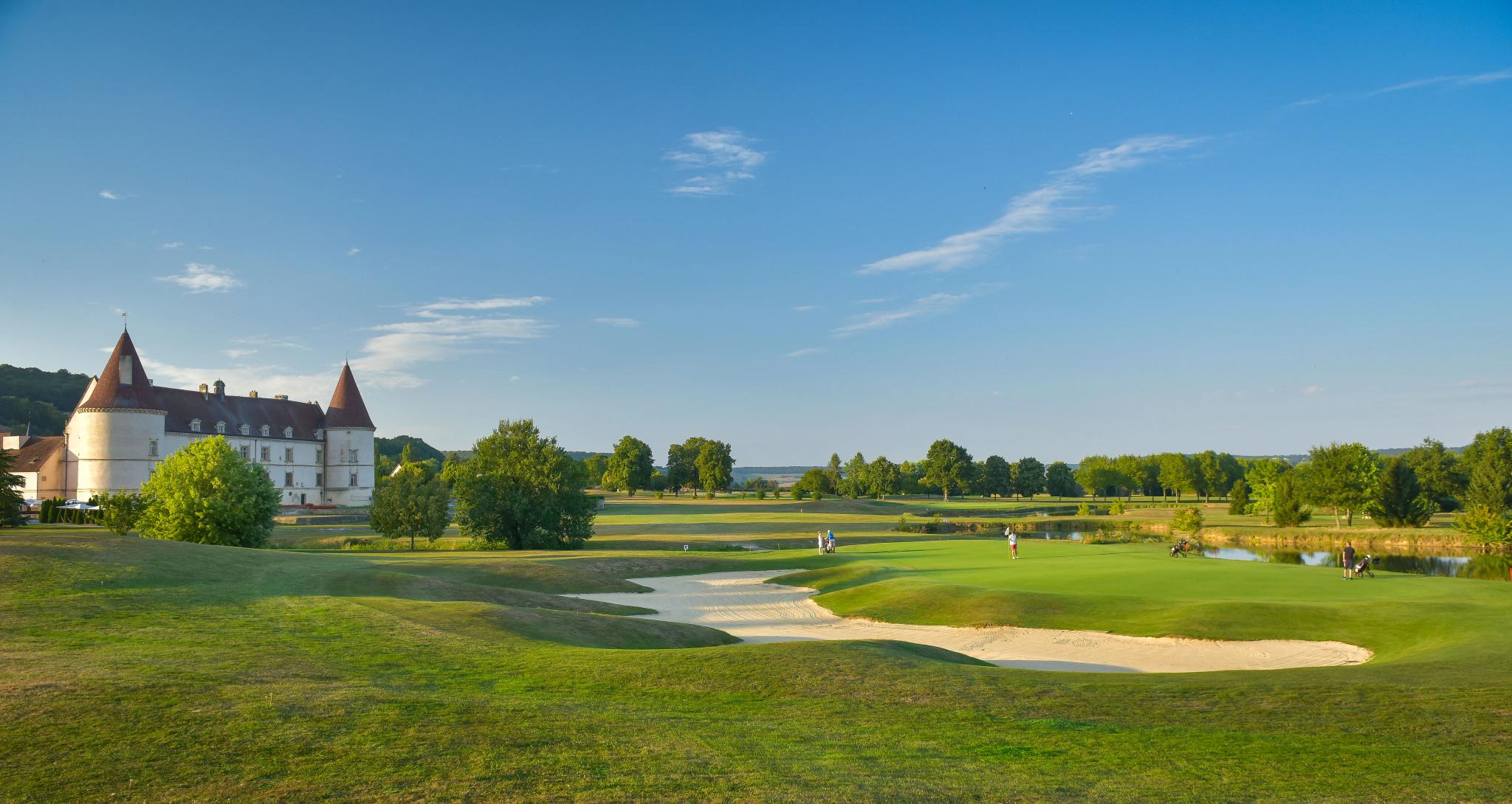 Wide view of the course with a large bunker surrounding a green with the hotel on the left