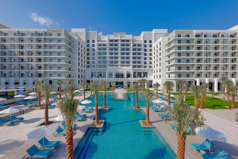 An outdoor swimming pool at the hotel surrounded by palm trees and sunbeds