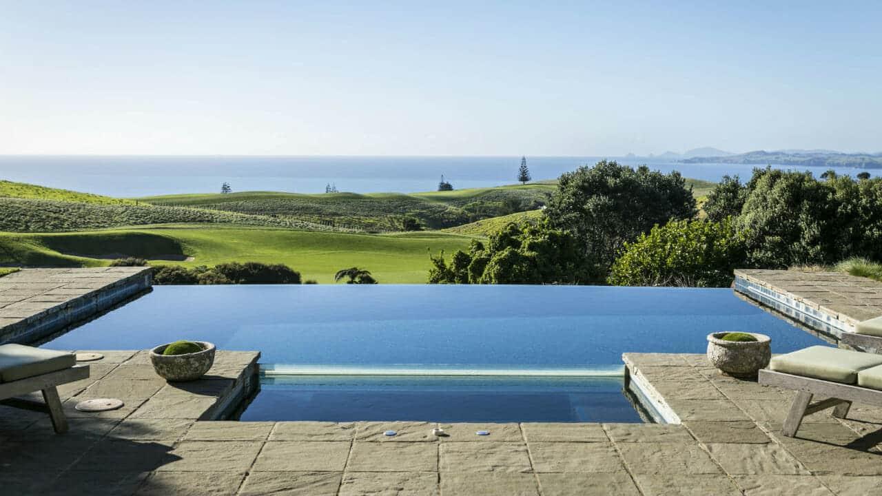 An outdoor swimming pool surrounded by sunbeds with coastal views