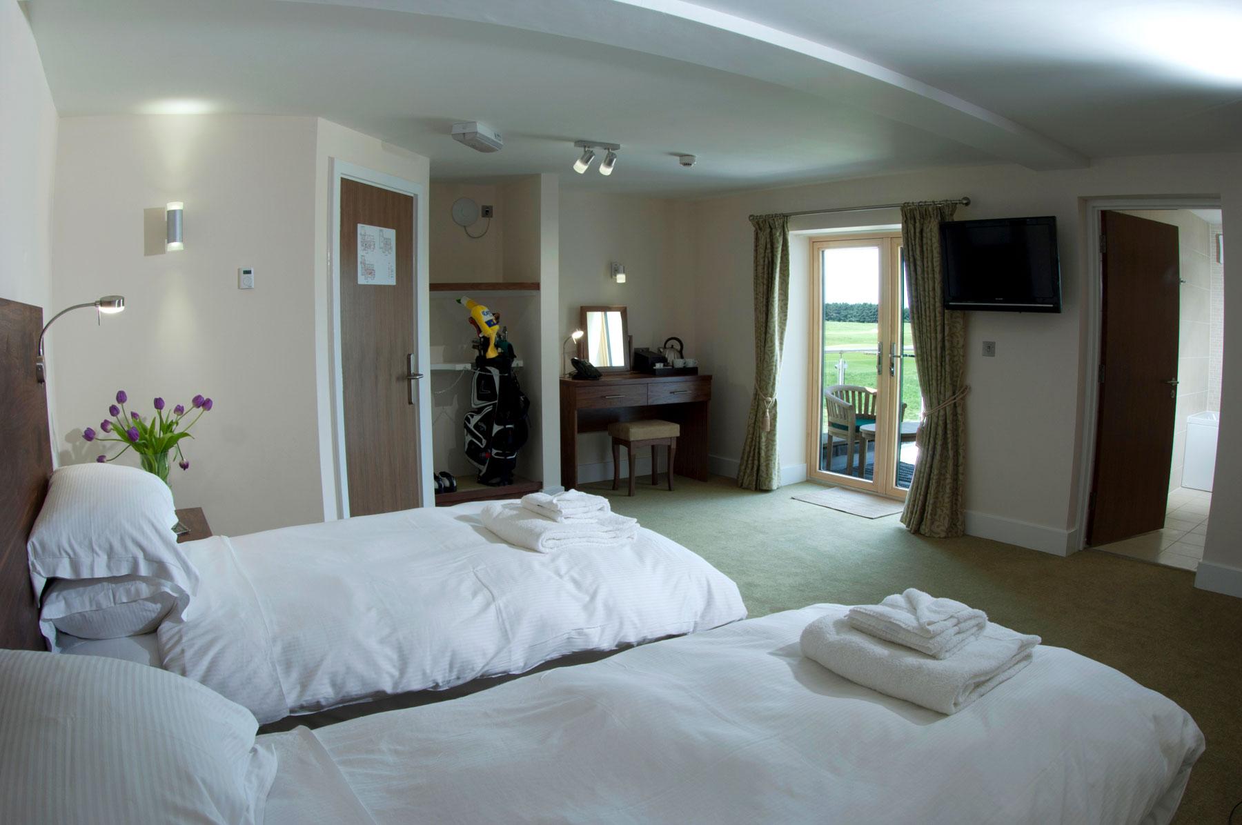Twin bed room at the hotel with seating on the patio and views of the course