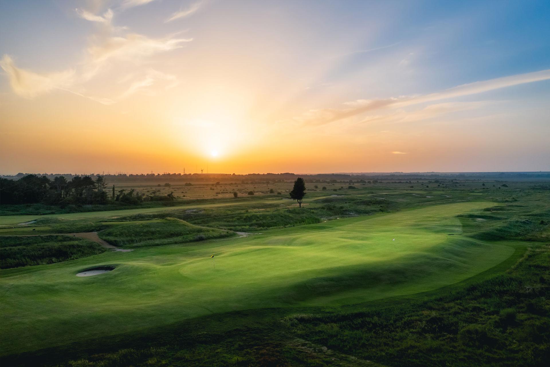 Sun setting over the manicured green with rolling dunes and littered trees