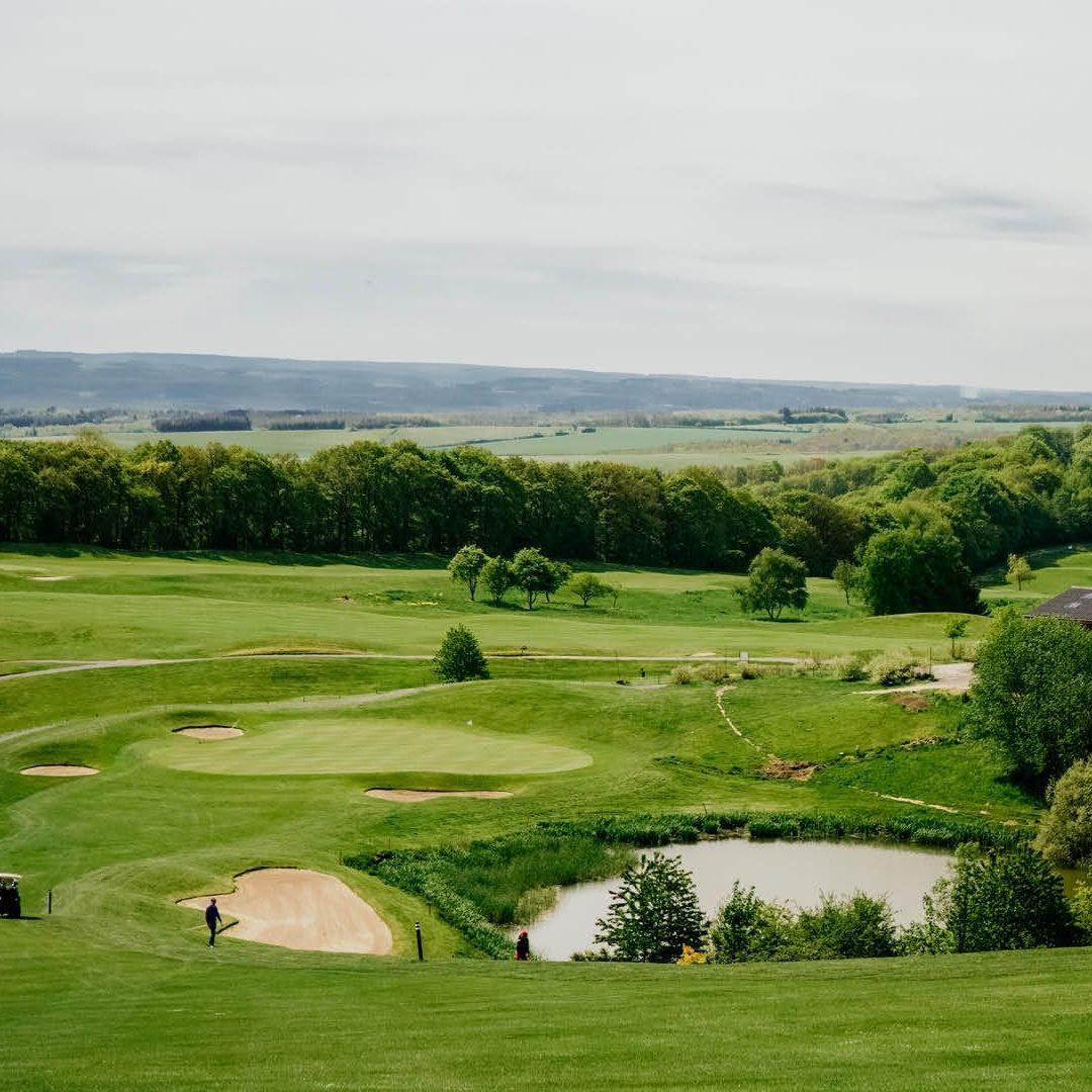 A smooth green nestled with sand bunkers next to a water hazard