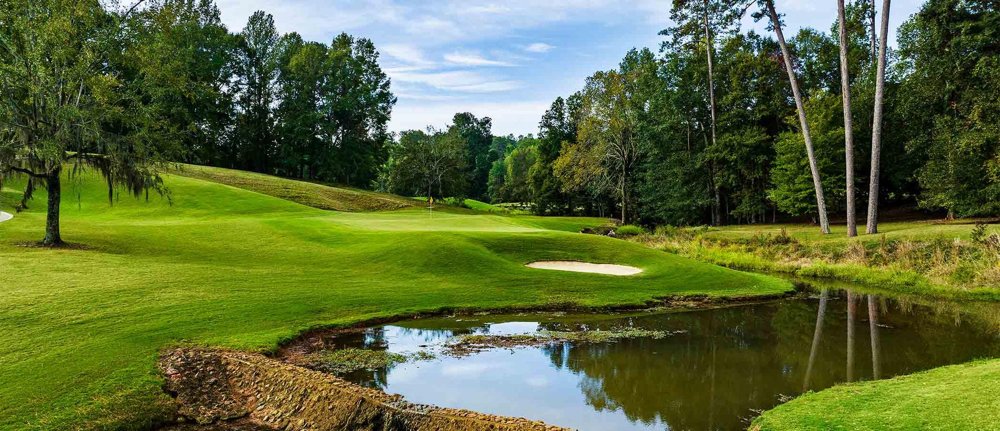 A sand bunker being sandwiched by a smooth green and water hazard