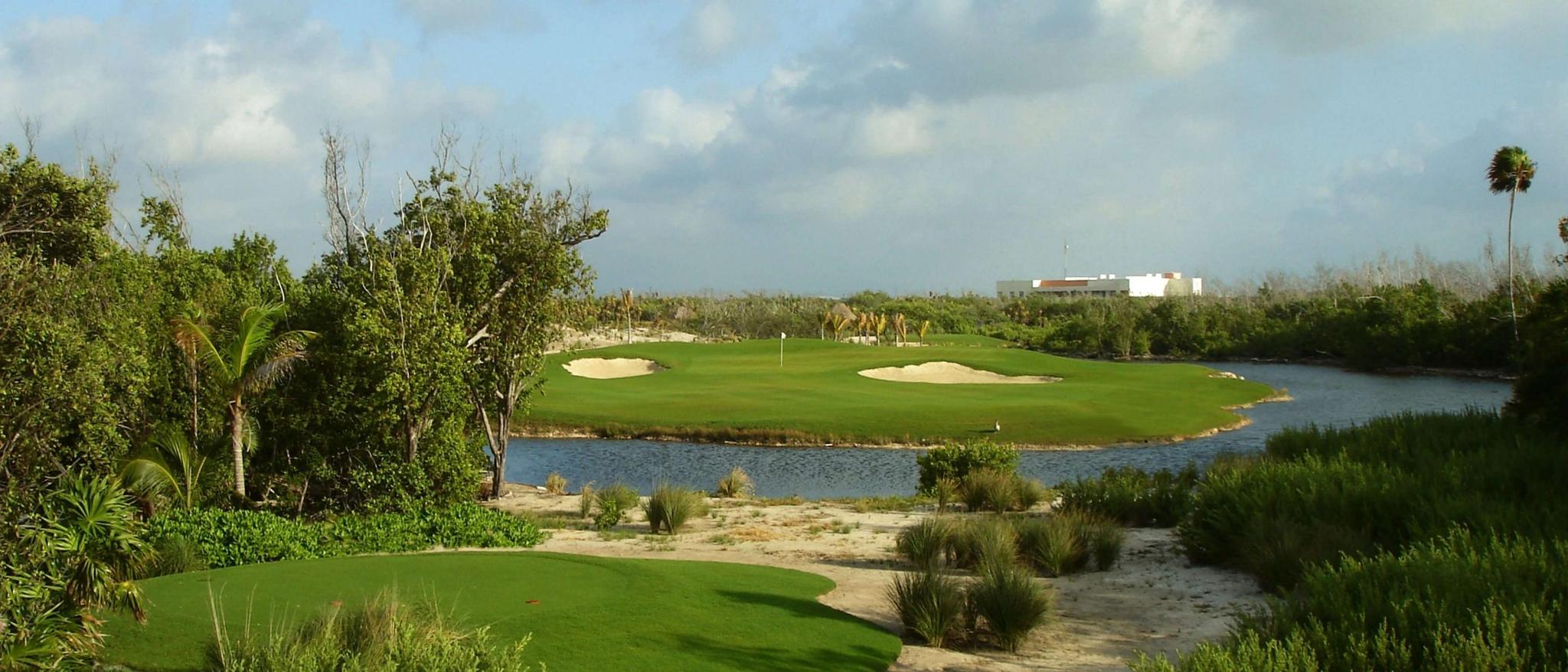 Panoramic view of a smooth green nestled with sand bunkers surrounded by a water hazard