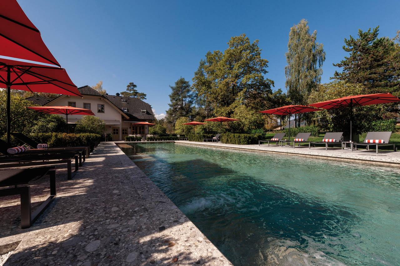 Outdoor swimming pool at the resort surrounded by sunbeds and red umbrellas