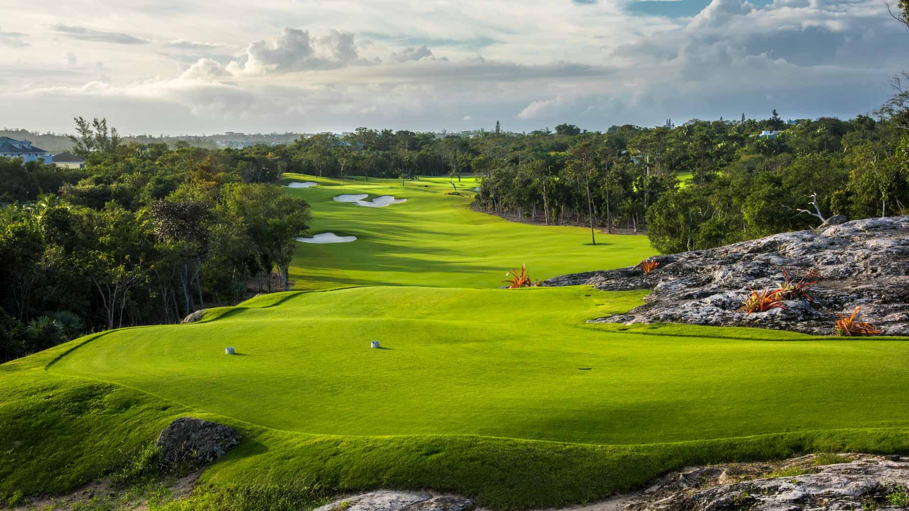 A lush fairway stretches through rocky terrain and dense trees.
