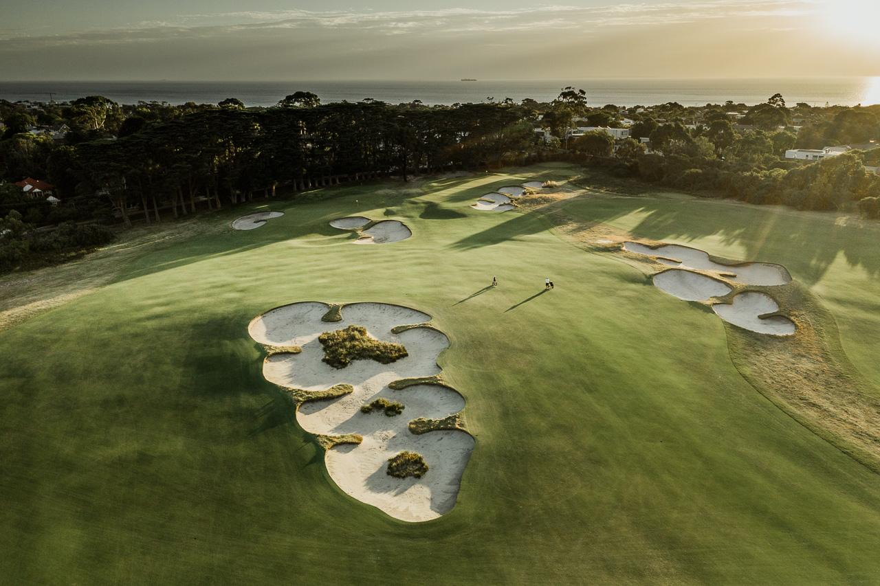 Overhead view of the sun setting over a sand bunker riddled fairway