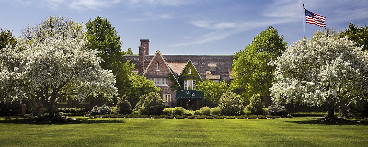 A springtime view of The American Club with blooming trees and a bright green lawn.