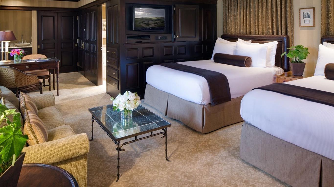 A spacious hotel room featuring two large beds and a sitting area.