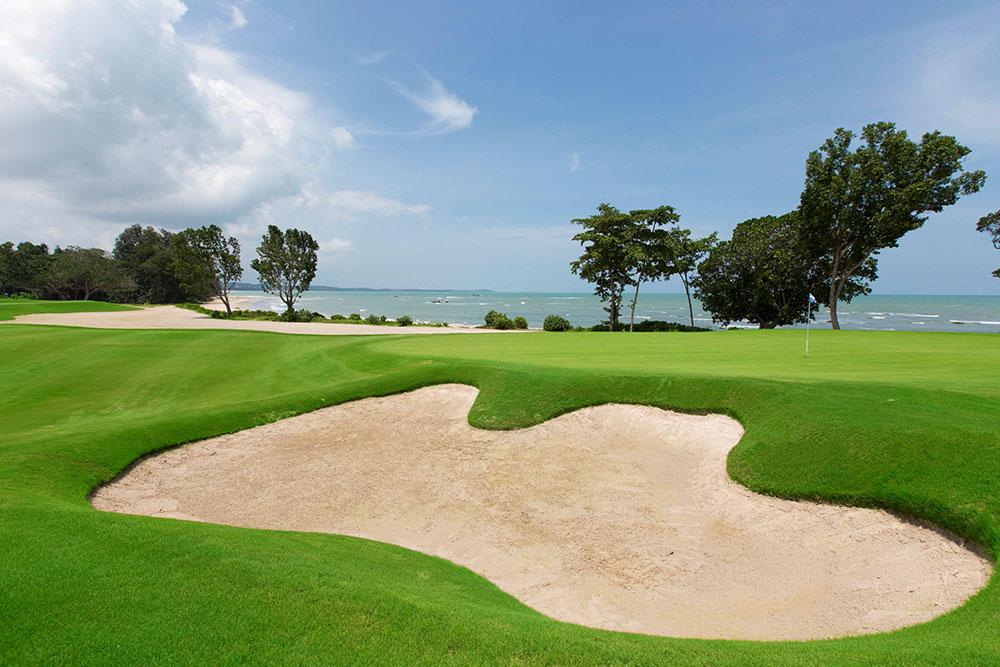 A sandy bunker and green located near the ocean shore.