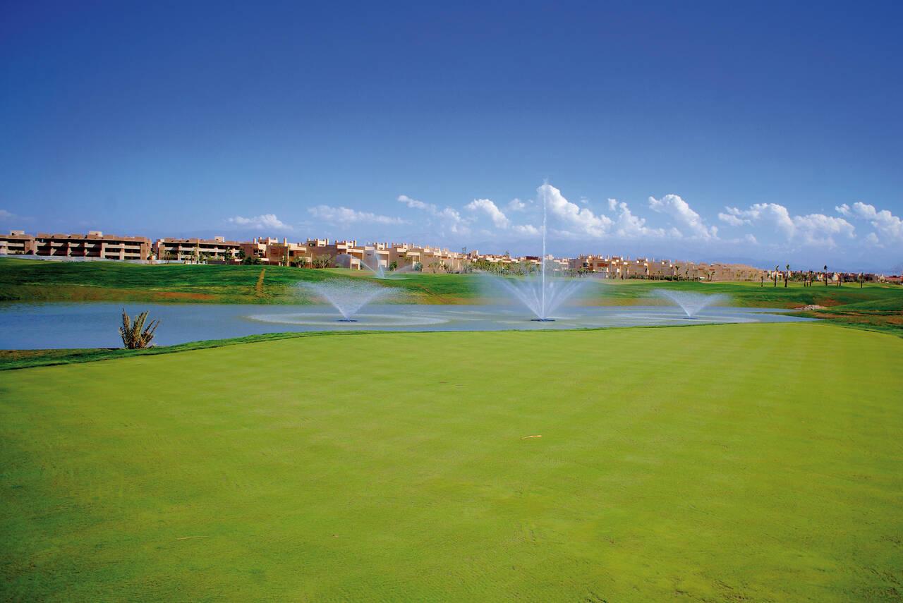 A water hazard with water fountains next to a well-kept green