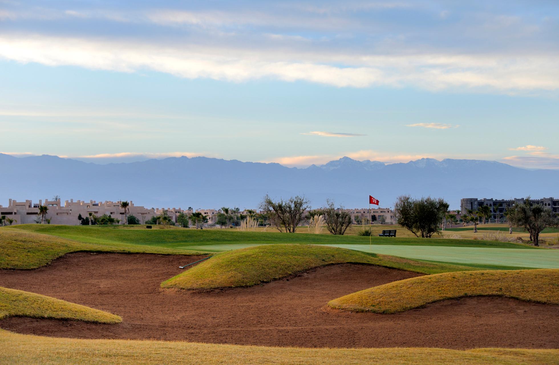 A smooth green placed next to a large sand bunker with mountain views in the background