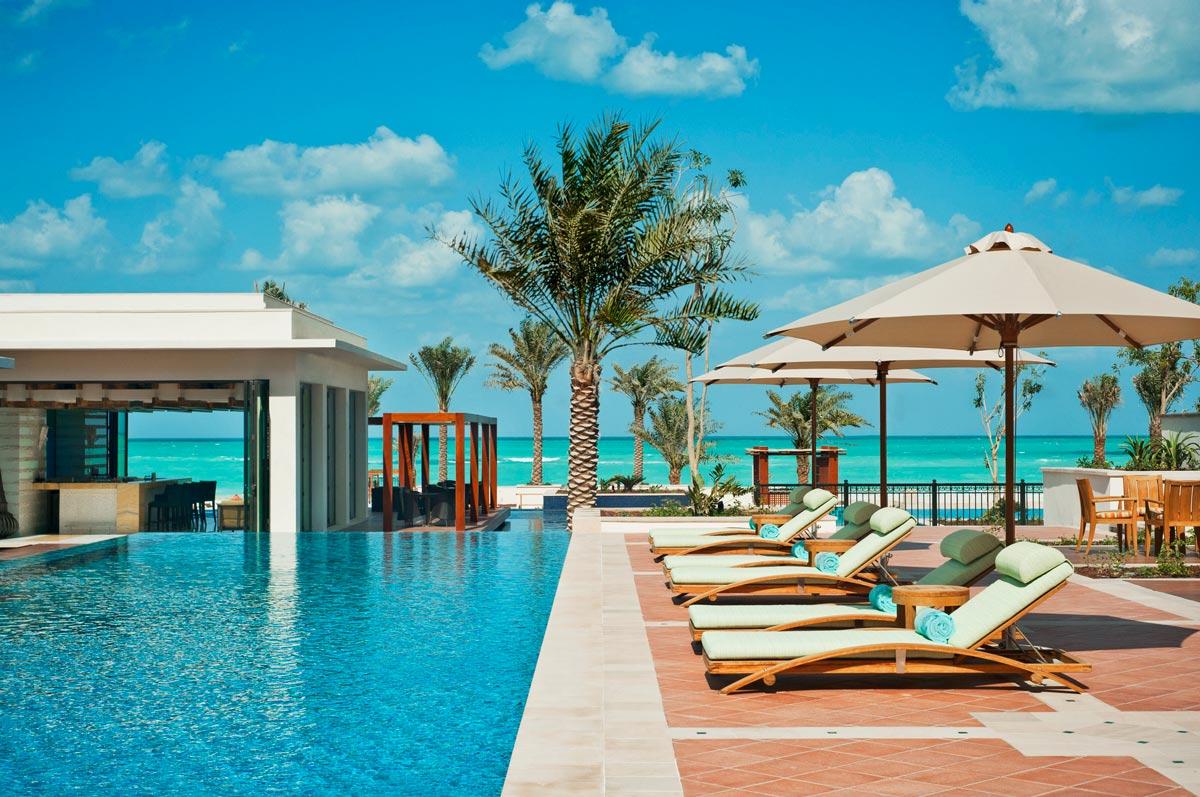 An outdoor swimming pool at the resort surrounded by sunbeds and palm trees