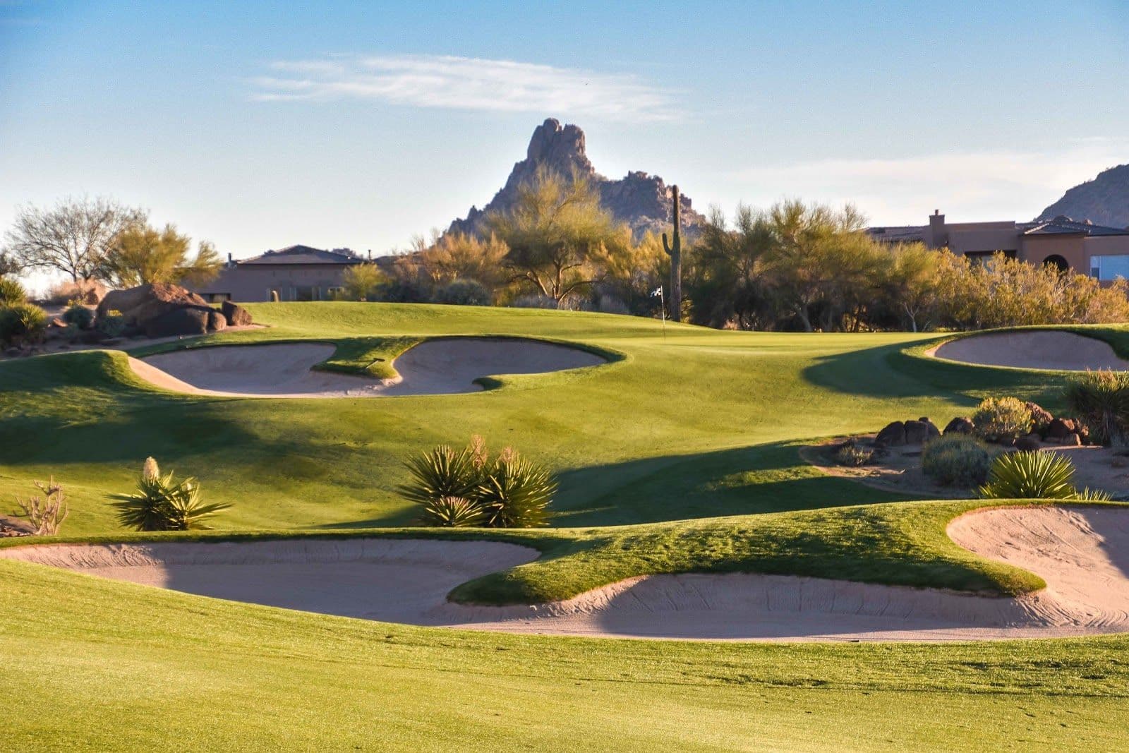 A green fairway with multiple sand bunkers leading up to the flag with desert mountains in the distance.