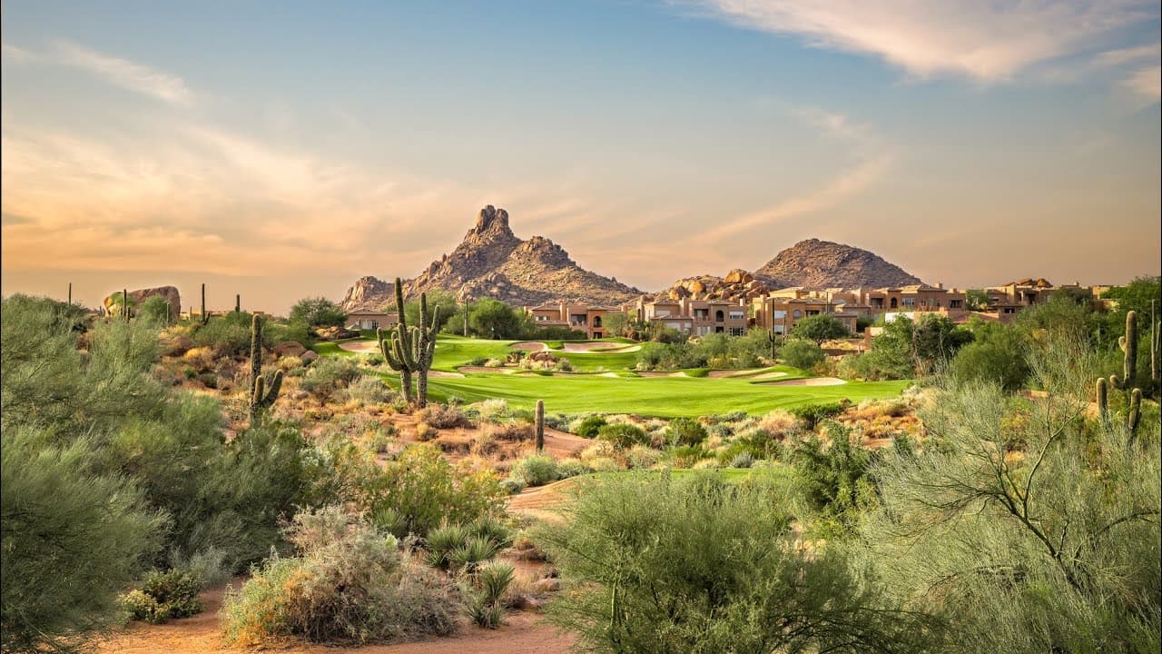 A scenic desert golf hole surrounded by vegetation and cacti with homes in the background.