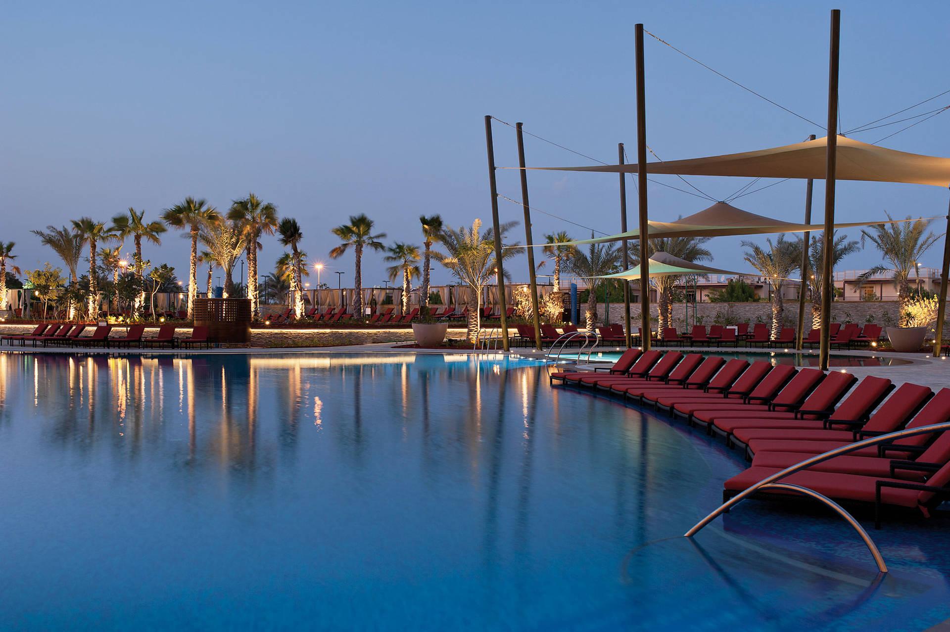 A outdoor swimming pool surrounded by red sunbeds and palm trees