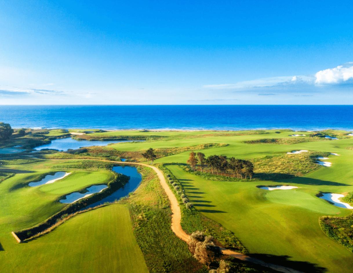 Expansive aerial view of the golf course with winding paths and water features near the sea.
