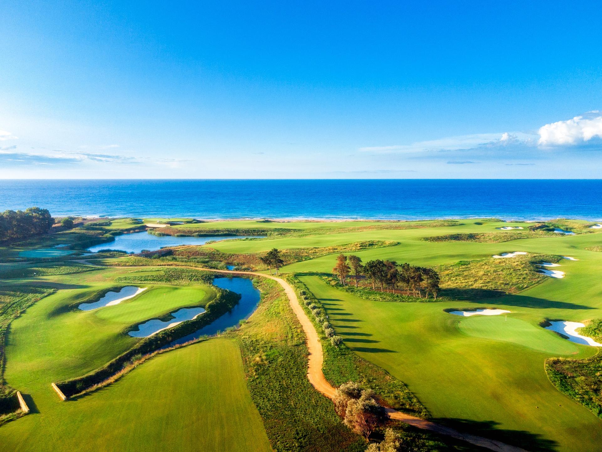 Expansive aerial view of the golf course with winding paths and water features near the sea.