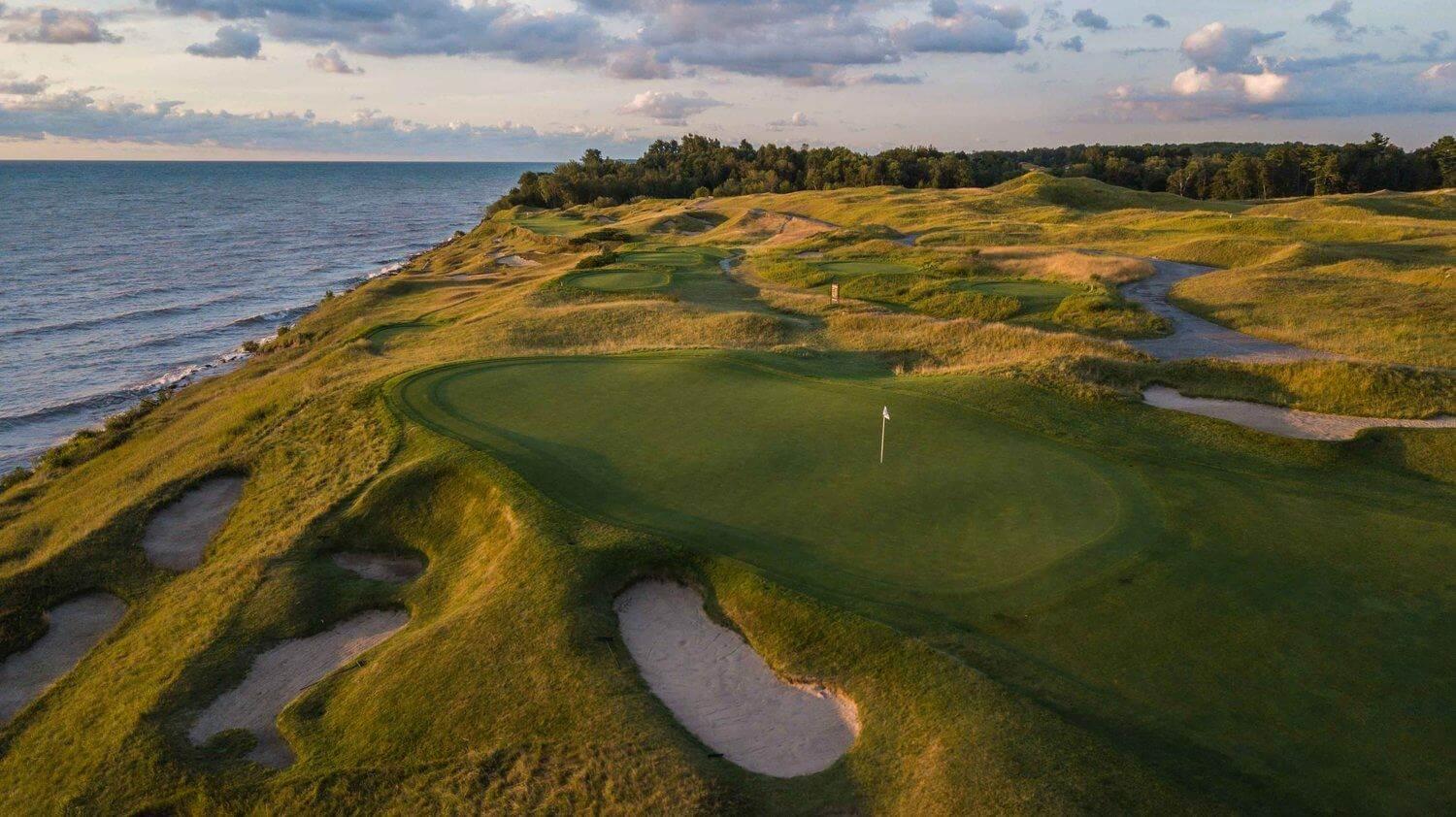 Overhead shot of a smooth green surrounded by sand bunkers in the rough with coastal views