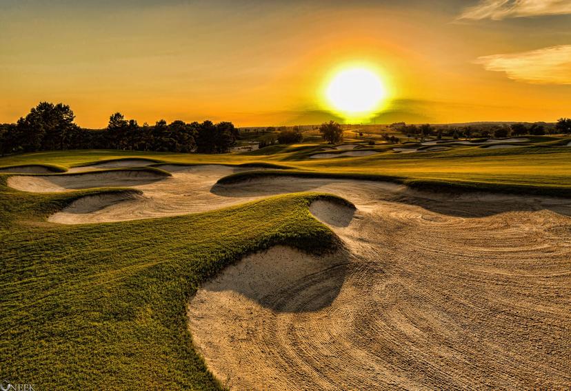 Sun setting over a large sand bunker surrounded by a well maintained fairway