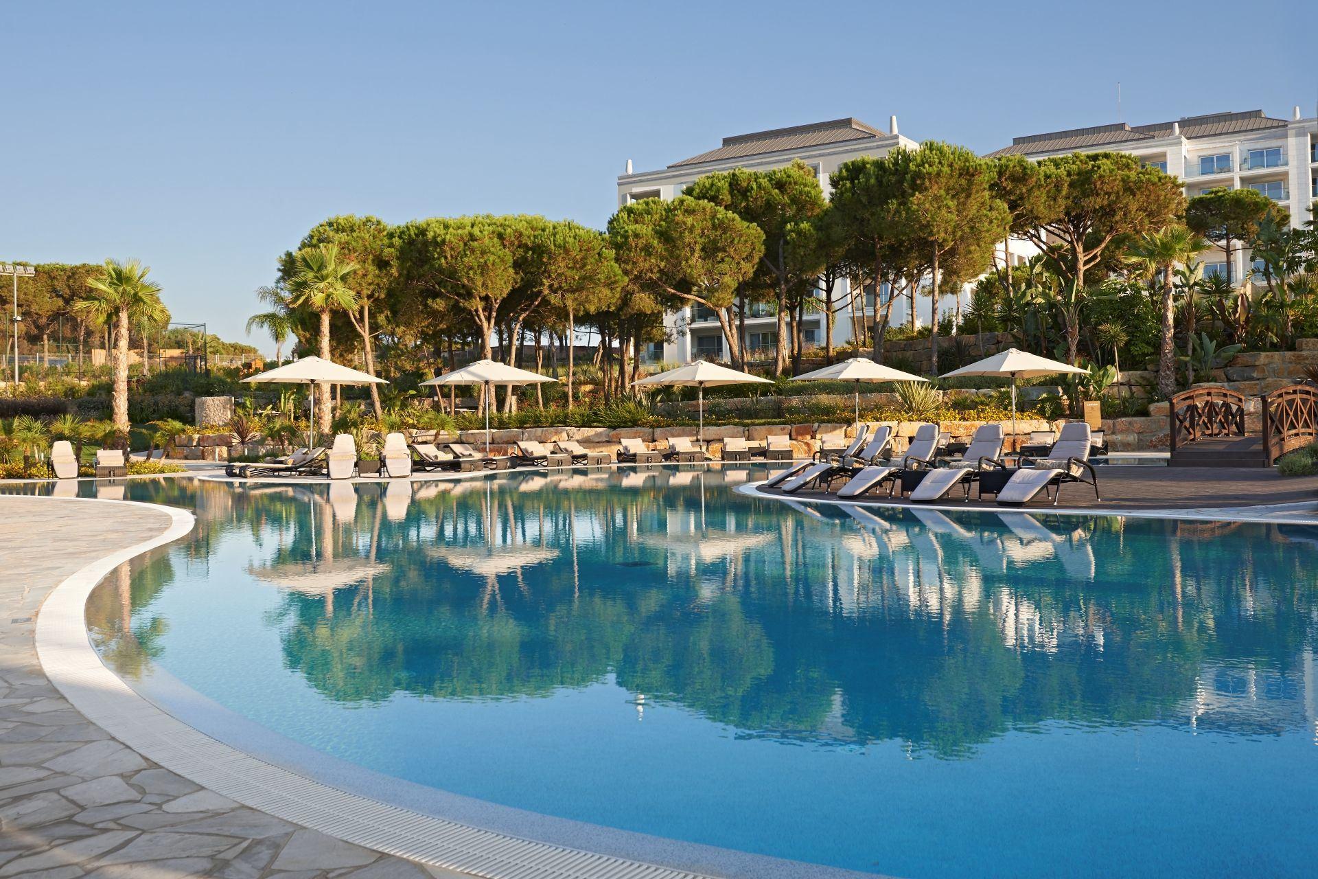 A serene pool reflecting the surrounding trees and umbrellas under clear blue skies