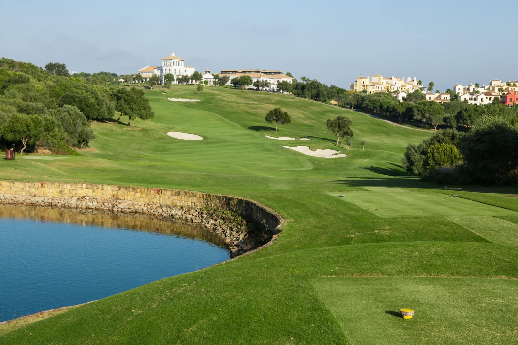A uphill fairway leading to a smooth green surrounded by sand bunkers with the clubhouse at the top of the hill
