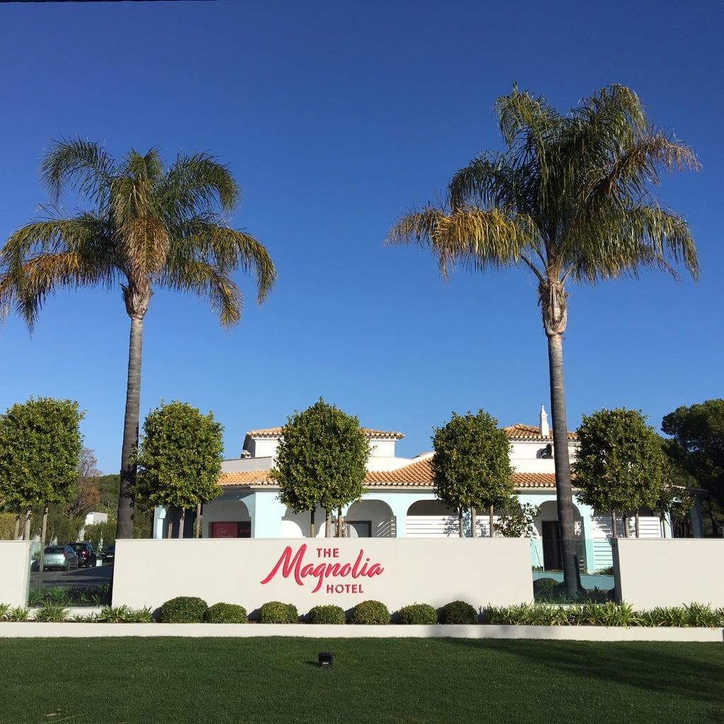 The Magnolia Hotel sign in pink writing at the front of the building with palm trees