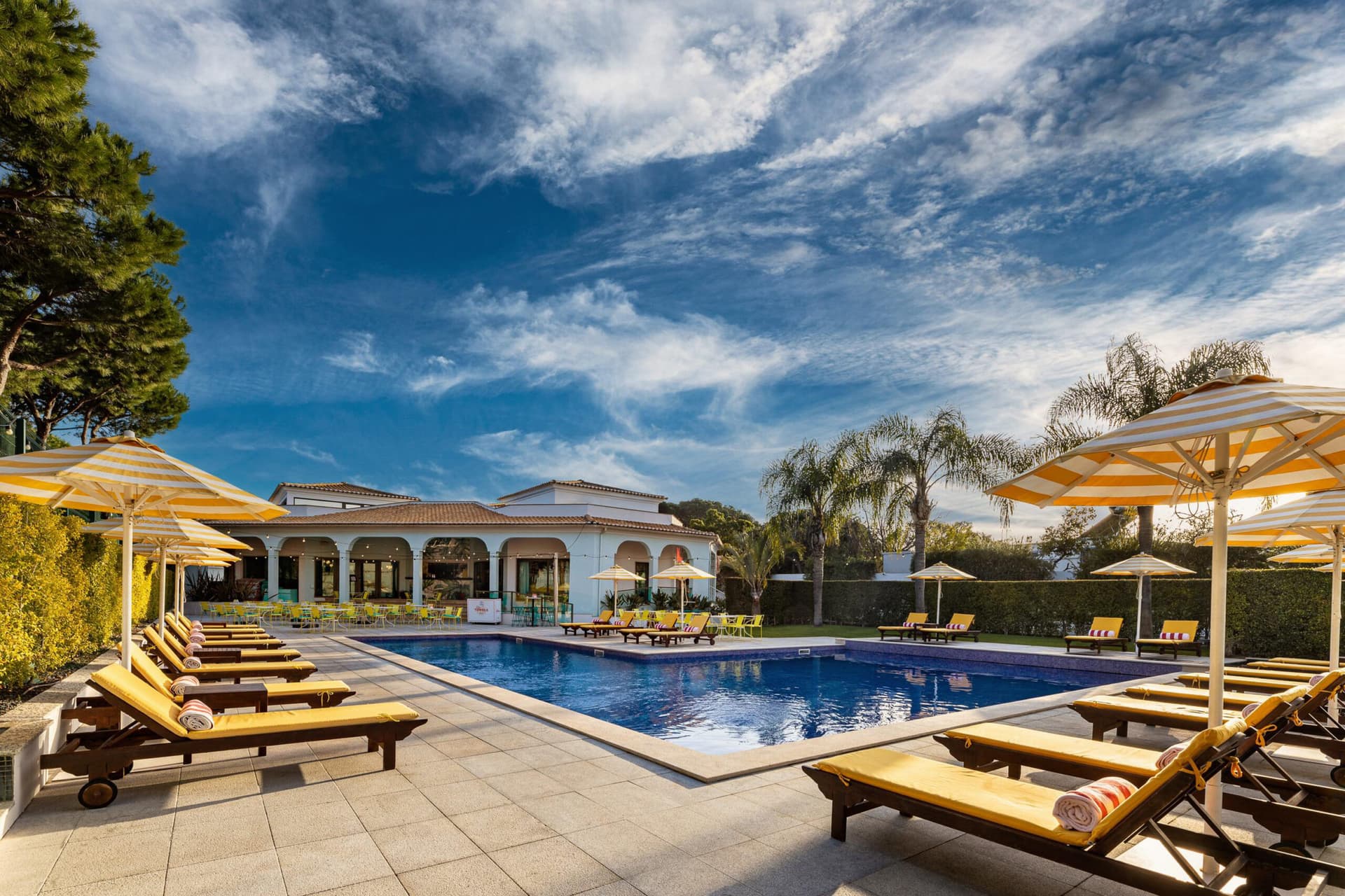 An outdoor swimming pool surrounded by yellow sunbeds with umbrellas